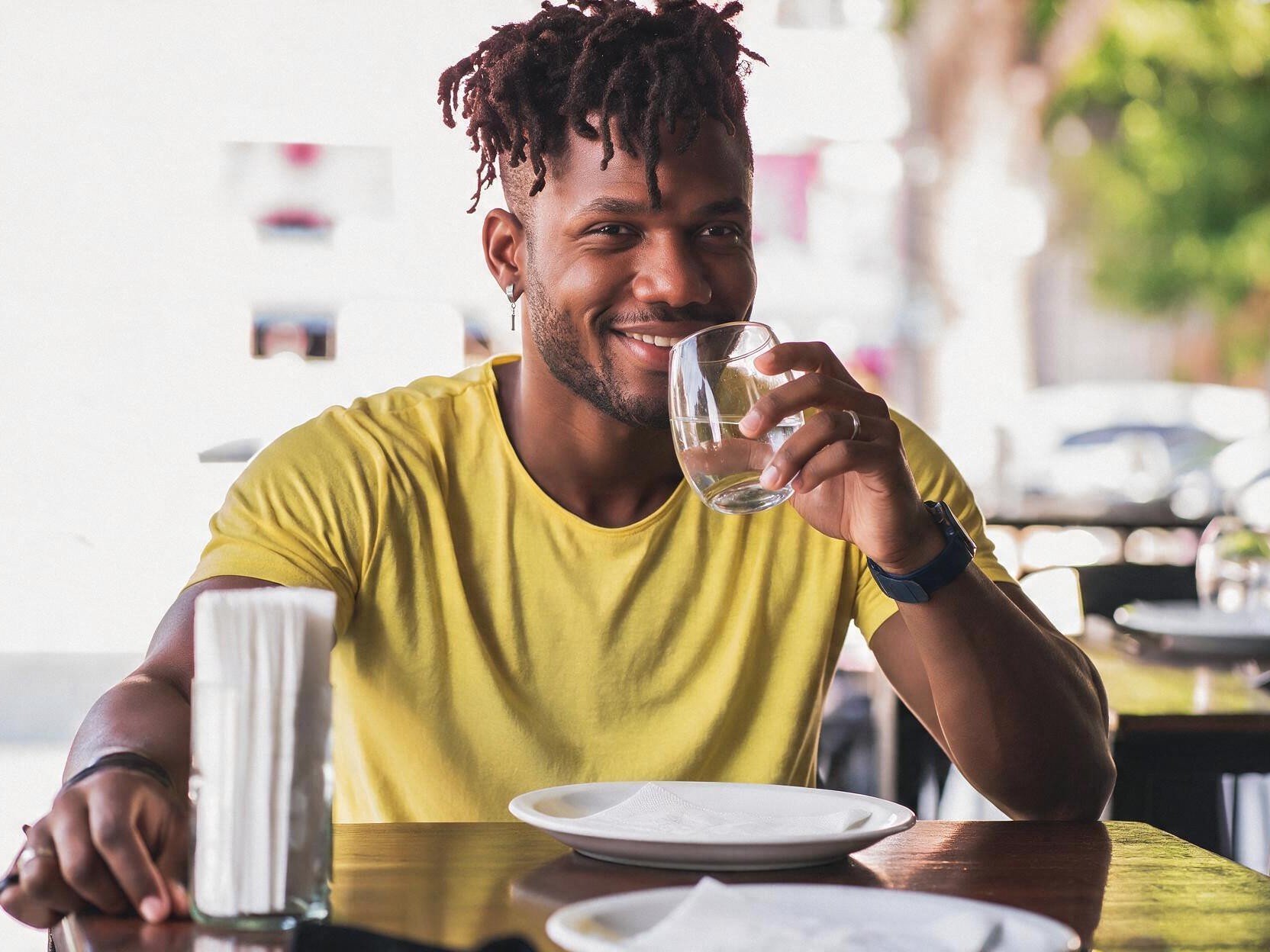 Man drinking a glass of water at an empty table